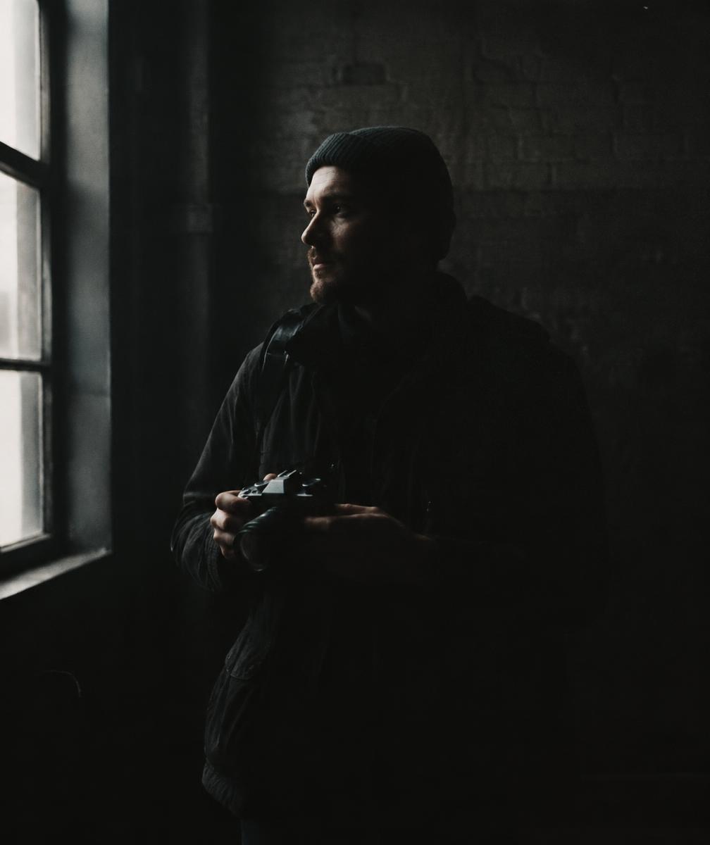 The photographer behind Deviant Lenses holding a camera in low window light