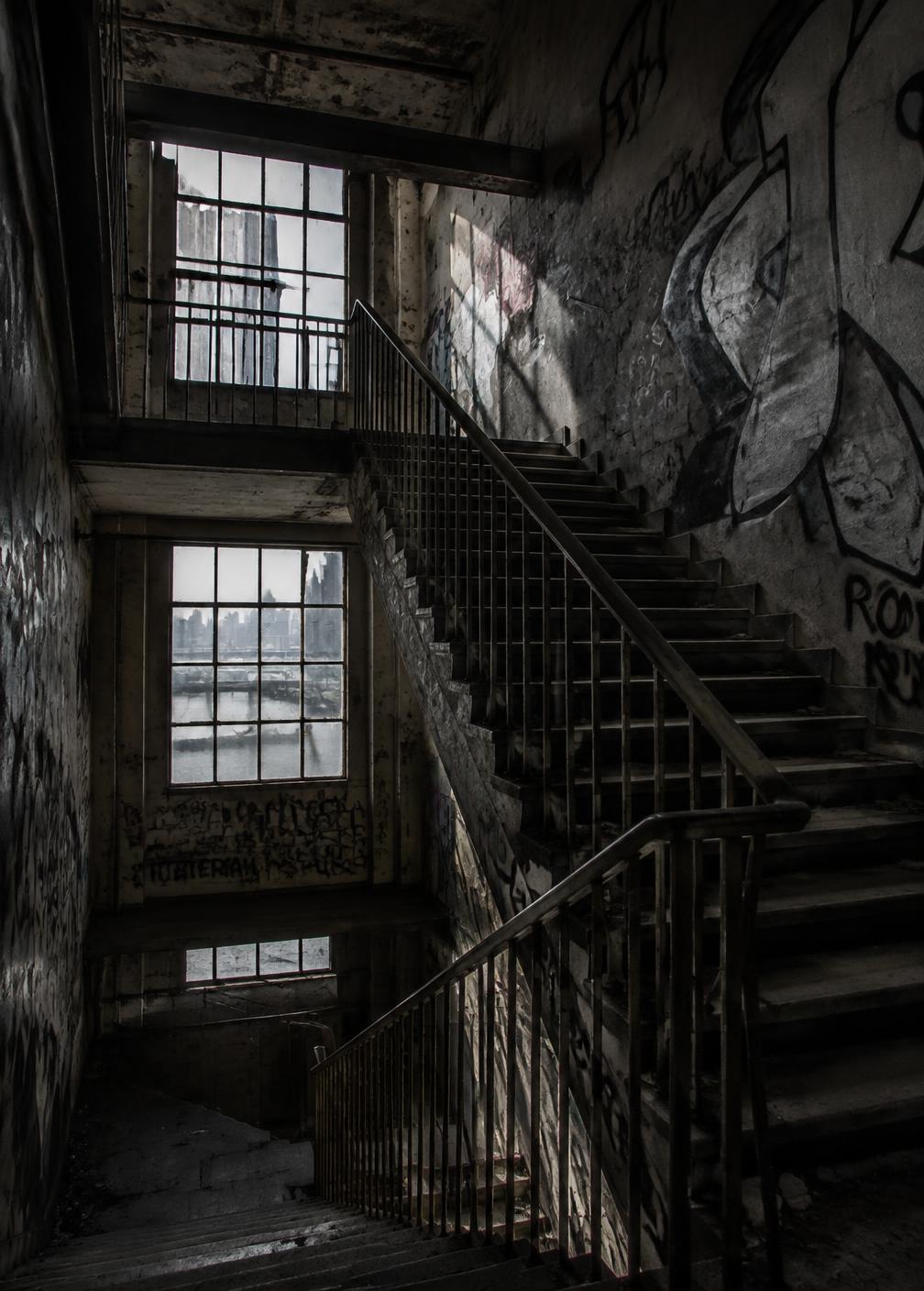Graffitied industrial stairwell in low light with pale daylight through a dirty window
